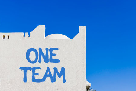 One team symbol. Concept word One team on beautiful white wall. Beautiful blue sky background. Business one team concept. Copy space.の写真素材