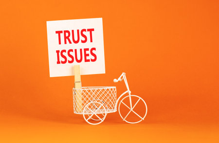 Trust issues symbol. Concept word Trust issues on beautiful white paper. Beautiful wooden clothespin. Miniature white bicycle. Beautiful orange background. Business trust issues concept. Copy space.の写真素材
