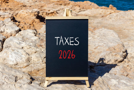 Taxes 2026 new year symbol. Concept words Taxes 2026 on beautiful black blackboard. Beautiful stone and blue sky background. Business and taxes 2026 new year concept. Copy space.の写真素材