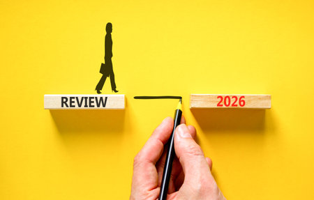 Review 2026 symbol. Concept words Review 2026 on beautiful wooden blocks. Beautiful yellow background. Businessman holds pencil. Businesswoman icon. Business and review 2026 concept. Copy space.の写真素材