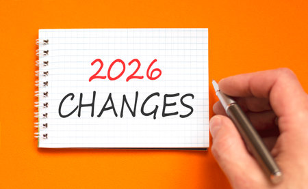 2026 Changes symbol. Concept words 2026 Changes on beautiful white note. Beautiful orange paper background. Businessman's hand with pen. Business and 2026 changes concept. Copy space.の写真素材