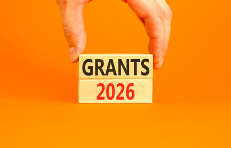 Grants 2026 symbol. Concept words Grants 2026 on beautiful wooden blocks. Beautiful orange paper background. Businessman's hand. Business and grants 2026 concept. Copy space.の写真素材