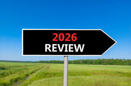 2026 Review symbol. Concept words 2026 Review on beautiful black road sign. Beautiful green grass field forest and blue sky background. Business and 2026 review concept. Copy space.の写真素材