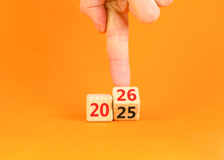 Business concept of 2026 new year symbol. Businessman turns wooden cube and changes number 2025 to 2026. Beautiful orange table orange background, copy space. Business 2026 happy new year concept.の写真素材
