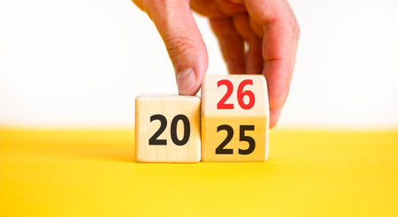 Business concept of 2026 new year symbol. Businessman turns wooden cube and changes number 2025 to...