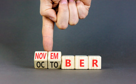 Symbol for the change from October to November. Businessman turns wooden cubes and changes the word October to November. Beautiful gray background. Copy space.の写真素材