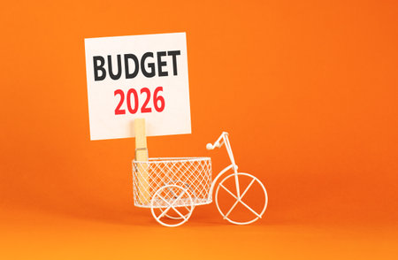 Budget 2026 symbol. Concept words Budget 2026 on beautiful white paper on wooden clothespin. Beautiful orange background. Beautiful miniature bicycle. Business and budget 2026 concept. Copy space.の写真素材