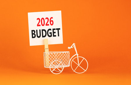 2026 Budget symbol. Concept words 2026 Budget on beautiful white paper on wooden clothespin. Beautiful orange background. Beautiful miniature bicycle. Business and 2026 budget concept. Copy space.の写真素材
