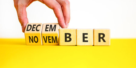 Symbol for the change from November to December. Businessman turns wooden cubes and changes the word November to December. Beautiful white and yellow background. Copy space.の写真素材