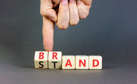 Brand or stand symbol. Concept words Brand Stand on beautiful wooden blocks. Beautiful gray background. Businessman's hand. Business brand or stand concept. Copy space.の写真素材