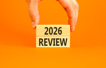 2026 Review symbol. Concept words 2026 Review on wooden blocks. Orange paper background. Businessman's hand. Business and 2026 review concept. Copy space.の写真素材