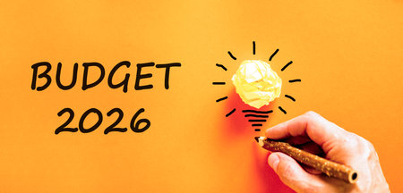 Budget 2026 symbol. Concept words Budget 2026 on beautiful orange paper. Beautiful orange paper background. Light bulb icon. Businessman's hand with pen. Business and budget 2026 concept. Copy space.の写真素材