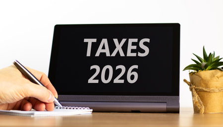 Taxes 2026 new year symbol. Concept words Taxes 2026 on beautiful black tablet screen. Beautiful white background. Businessman's hand. Business and taxes 2026 new year concept. Copy space.の写真素材