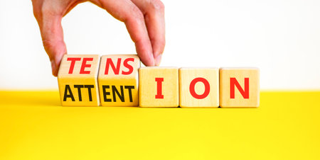 Tension or attention symbol. Concept words Attention or Tension on beautiful wooden blocks. Beautiful white and yellow background. Businessman's hand. Business tension or attention concept. Copy spaceの写真素材