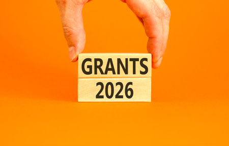 Grants 2026 symbol. Concept words Grants 2026 on beautiful wooden blocks. Beautiful orange paper background. Businessman's hand. Business and grants 2026 concept. Copy space.の写真素材