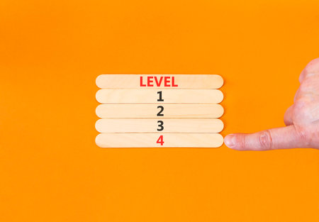 Time to level 4 symbol. Concept word Level 1 2 3 4 on beautiful wooden sticks. Businessman's hand. Beautiful orange background. Business planning and time to level 4 concept. Copy space.の写真素材