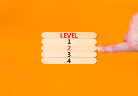 Time to level 2 symbol. Concept word Level 1 2 3 4 on beautiful wooden sticks. Businessman's hand. Beautiful orange background. Business planning and time to level 2 concept. Copy space.の写真素材