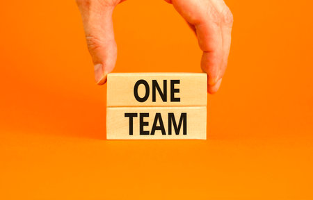 One team symbol. Concept word One team on beautiful wooden blocks. Beautiful orange paper background. Businessman's hand. Business one team concept. Copy space.の写真素材