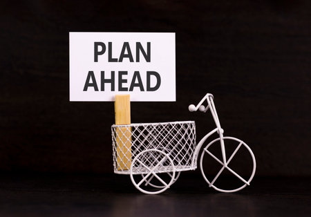 Plan ahead symbol. Concept word Plan ahead on beautiful white paper. Beautiful wooden clothespin. Miniature white bicycle. Beautiful black background. Business plan ahead concept. Copy space.の写真素材
