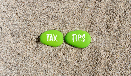 Tax tips symbol. Concept word Tax tips on beautiful green stones. Sea sand beach. Beautiful sand beach background. Business tax tips concept. Copy space.の写真素材