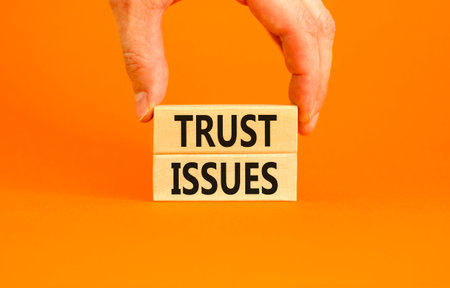 Trust issues symbol. Concept word Trust issues on beautiful wooden blocks. Beautiful orange paper background. Businessman's hand. Business trust issues concept. Copy space.の写真素材
