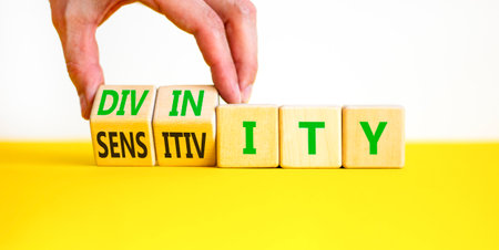 Sensitivity or divinity symbol. Concept words Sensitivity or Divinity on wooden cubes. Beautiful white and yellow background. Psychologist hand. Psychology sensitivity or divinity concept. Copy space.の写真素材