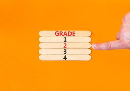 Time to grade 2 symbol. Concept word Grade 1 2 3 4 on beautiful wooden sticks. Businessman's hand. Beautiful orange background. Business planning and time to grade 2 concept. Copy space.の写真素材