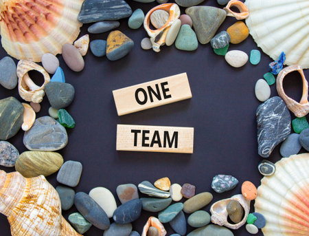 One team symbol. Concept word One team on beautiful wooden blocks. Beautiful black paper background. Beautiful sea stones and sea shells. Business one team concept. Copy space.の写真素材