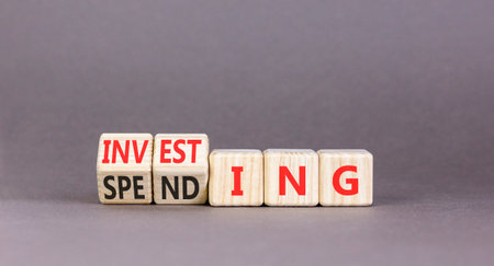 Investing and spending symbol. Concept words Spending to Investing on beautiful wooden cubes. Beautiful gray table gray background. Business, investing and spending concept. Copy space.の写真素材