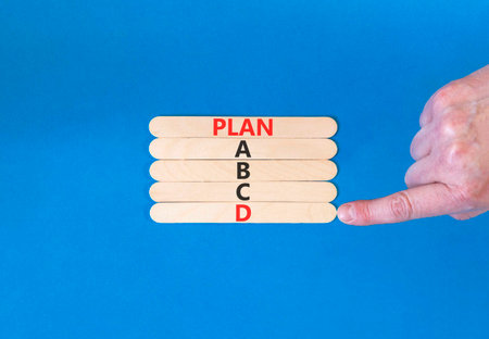 Time to plan D symbol. Concept word Plan ABCD on beautiful wooden sticks. Businessman's hand. Beautiful blue background. Business planning and time to plan D concept. Copy space.の写真素材