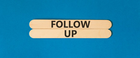 Follow up symbol. Concept word Follow up on beautiful wooden sticks. Beautiful blue paper background. Business follow up concept. Copy space.の写真素材