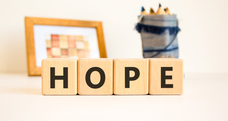 Hope symbol. Concept word Hope on beautiful wooden blocks. Beautiful picture frame and colored pencils. Beautiful white table white background. Business, lifestyle, support hope concept. Copy space.の写真素材