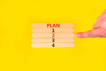 Time to plan 2 symbol. Concept word Plan 1 2 3 4 on beautiful wooden sticks. Businessman's hand. Beautiful yellow background. Business planning and time to plan 2 concept. Copy space.の写真素材