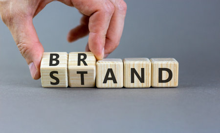 Brand or stand symbol. Concept words Brand Stand on beautiful wooden blocks. Beautiful gray background. Businessman's hand. Business brand or stand concept. Copy space.の写真素材