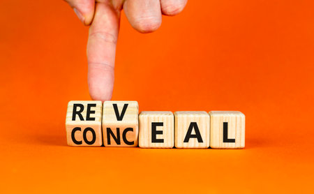Reveal or conceal symbol. Businessman turns wooden cubes and changes word Conceal to Reveal. Beautiful orange table orange background, copy space. Business reveal or conceal concept.の写真素材