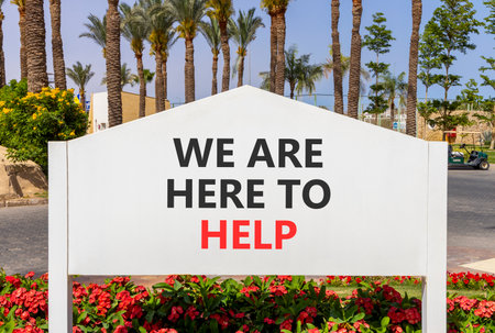 Support, help and we are here to help symbol. Concept words We are here to help on beautiful white road sign. Beautiful palm trees blue sky background. Business we are here to help concept. Copy spaceの写真素材