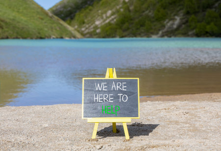 Support, help and we are here to help symbol. Concept words We are here to help on beautiful blackboard. Beautiful mountain lake background. Business we are here to help concept. Copy space.の写真素材
