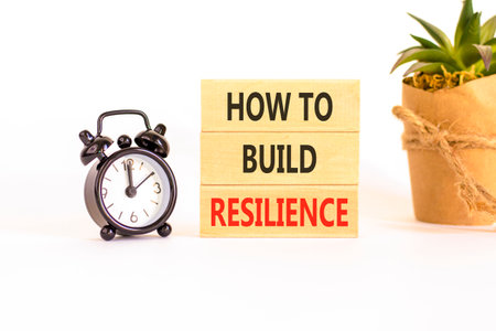 How to build resilience symbol. Concept words How to build resilience on beautiful wooden blocks. Beautiful white background. Black alarm clock. Business how to build resilience concept. Copy spaceの写真素材