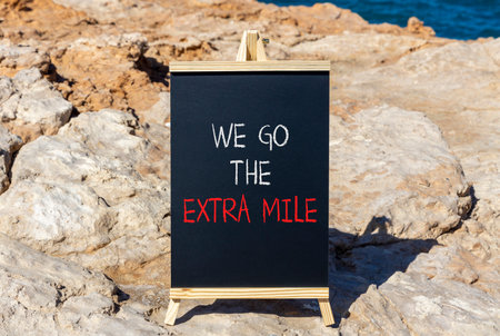 Support, help we go the extra mile symbol. Concept words We go the extra mile on beautiful blackboard. Beautiful stone and blue sky, sea background. Business we go the extra mile concept. Copy space.の写真素材