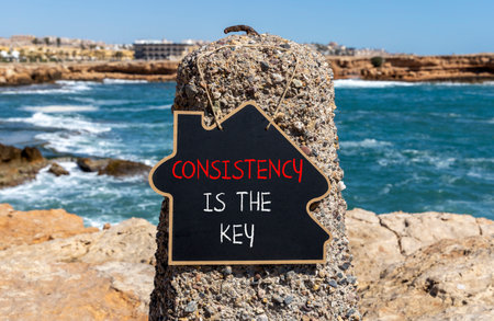 Consistency is the key symbol. Concept words Consistency is the key on beautiful blackboard. Beautiful stone and blue sky, sea background. Business consistency is the key concept. Copy space.の写真素材