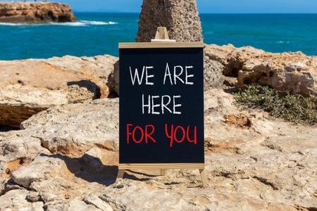 Support, help and we are here for you symbol. Concept words We are here for you on beautiful blackboard. Beautiful stone and blue sky, sea background. Business we are here for you concept. Copy space.の写真素材