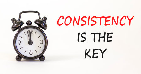 Consistency is the key symbol. Concept words Consistency is the key on beautiful white paper. Beautiful white paper background. Black alarm clock. Business consistency is the key concept. Copy space.の写真素材