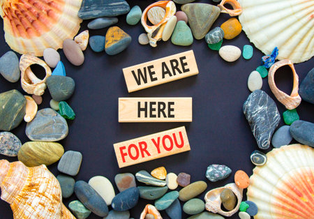 Support, help and we are here for you symbol. Concept words We are here for you on beautiful wooden blocks. Beautiful black background. Sea shells. Business we are here for you concept. Copy space.の写真素材