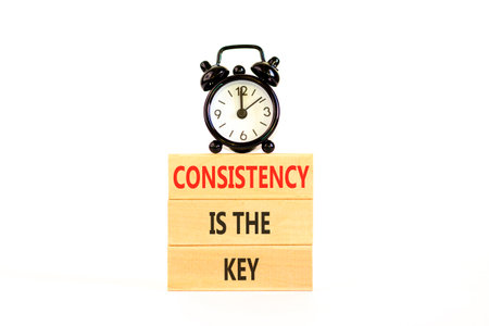Consistency is the key symbol. Concept words Consistency is the key on beautiful wooden blocks. Beautiful white background. Black alarm clock. Business consistency is the key concept. Copy space.の写真素材