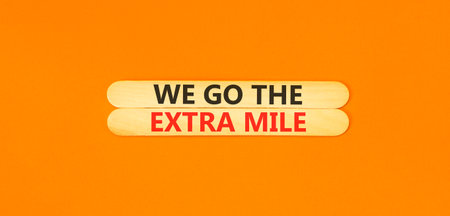 Support, help we go the extra mile symbol. Concept words We go the extra mile on beautiful wooden sticks. Beautiful orange background. Business we go the extra mile concept. Copy space.の写真素材