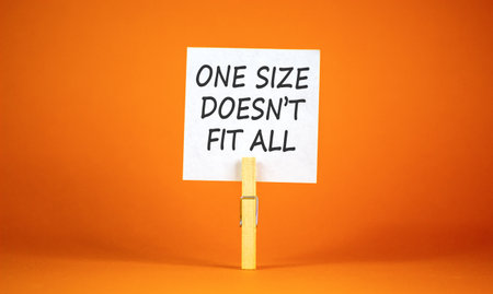 One size does not fit all symbol. Concept words One size does not fit all on beautiful white paper on clothespins. Beautiful orange background. Business one size does not fit all concept. Copy space.の写真素材