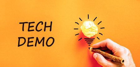 Tech demo symbol. Concept word Tech demo on beautiful orange paper. Businessman's hand. Light bulb...