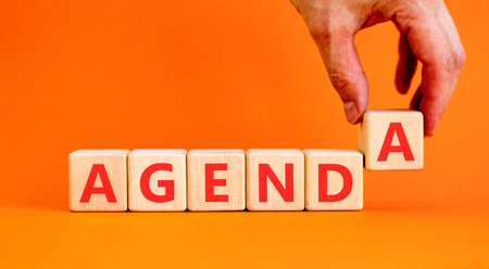 Agenda symbol. Concept word Agenda on beautiful wooden blocks. Beautiful orange background. Businessman's hand. Business agenda concept. Copy space.の写真素材