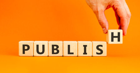 Publish word symbol. Concept word Publish on beautiful wooden blocks. Beautiful orange background. Businessman's hand. Business publish word concept. Copy space.の写真素材