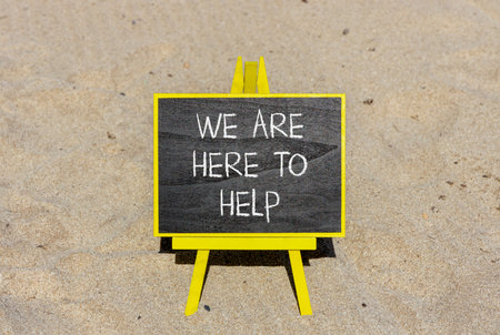 Support, help and we are here to help symbol. Concept words We are here to help on beautiful blackboard. Beautiful sand beach background. Business we are here to help concept. Copy space.の写真素材